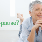 middle age white woman lying on her stomach on the floor, up on her elbows smiling with the words Menopause to ther right.